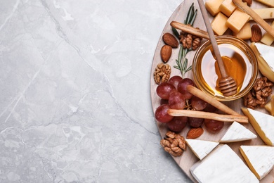 Photo of Cheese plate with honey, grapes and nuts on light grey marble table, top view. Space for text