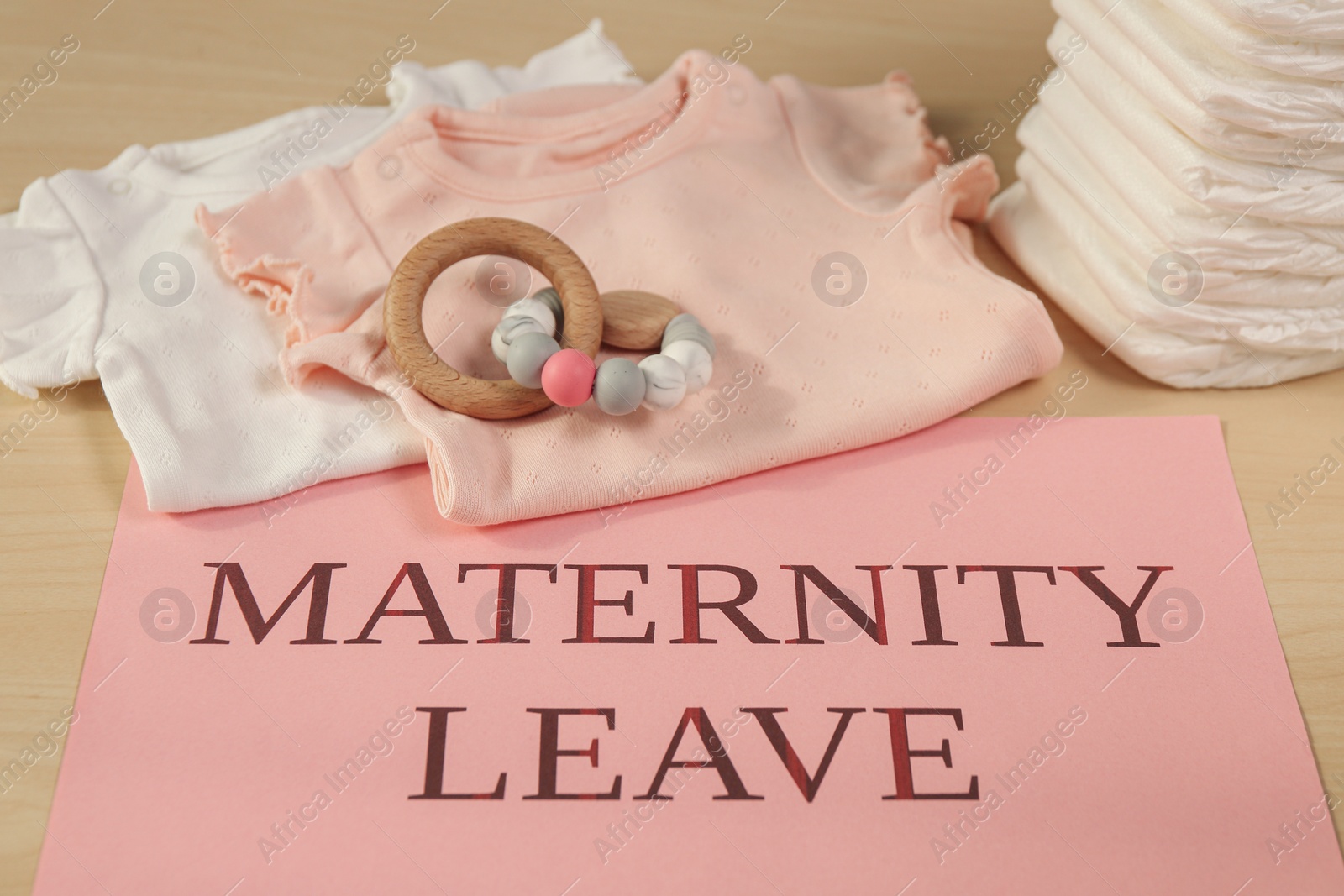 Photo of Baby clothes, toy, diapers and note with text Maternity Leave on wooden table
