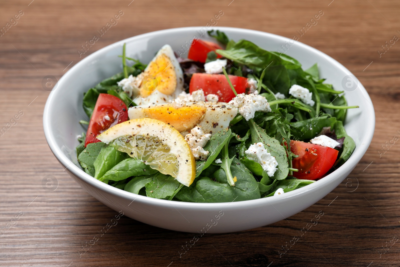 Photo of Delicious salad with boiled egg, tomatoes and cheese in bowl on wooden table, closeup