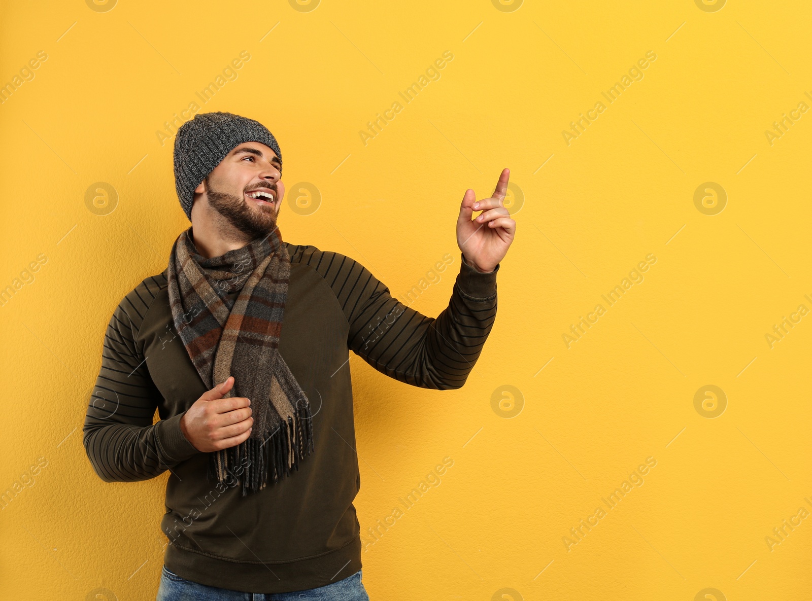 Photo of Happy young man in warm clothes on yellow background, space for text. Winter vacation