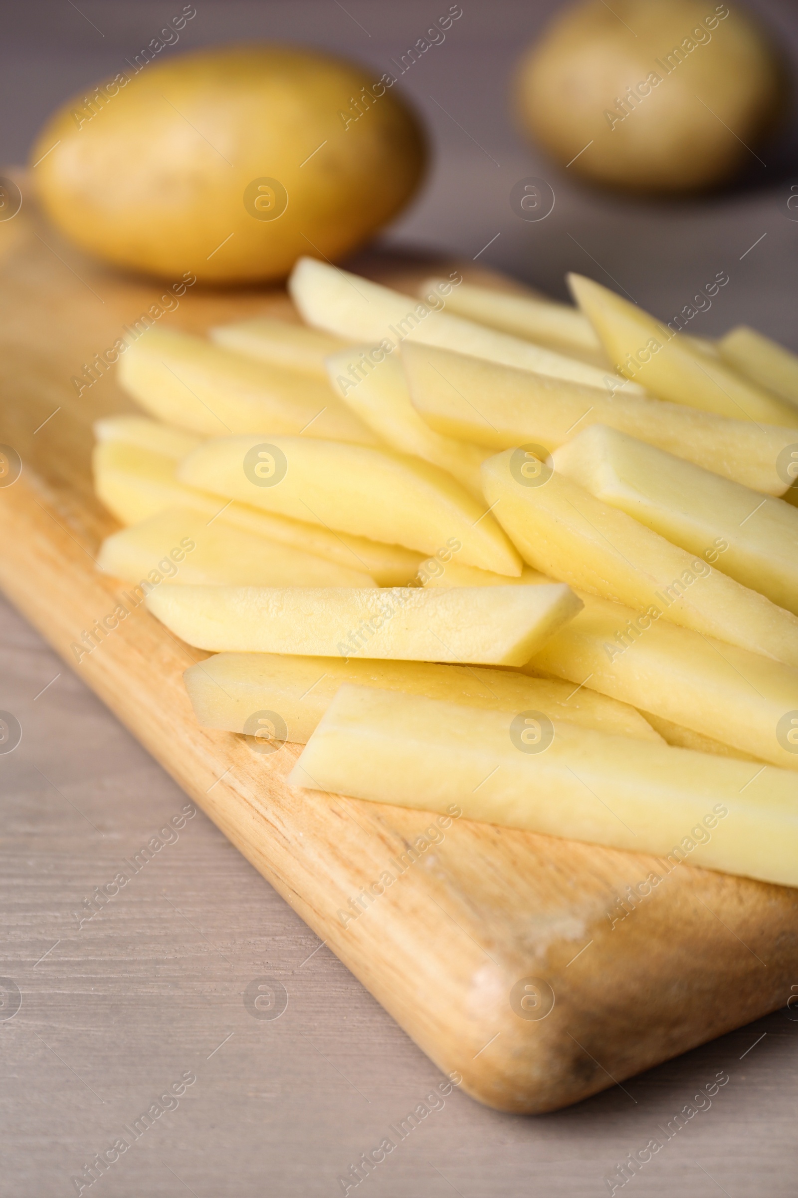 Photo of Whole and cut raw potatoes on wooden board, closeup