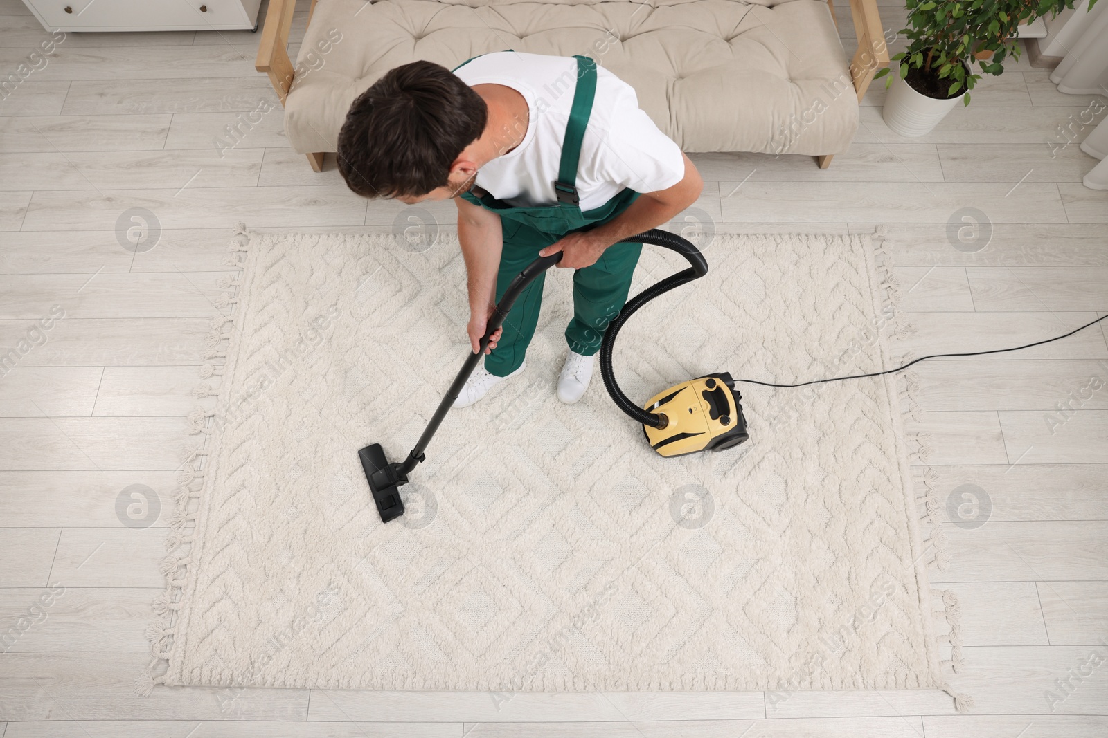 Photo of Dry cleaner's employee hoovering carpet with vacuum cleaner indoors, above view