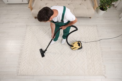 Dry cleaner's employee hoovering carpet with vacuum cleaner indoors, above view