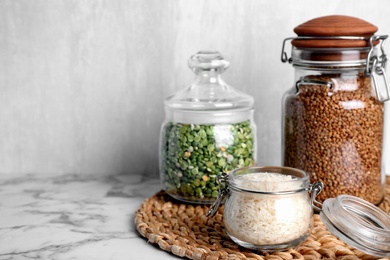 Glass jars with different types of groats on white marble table. Space for text