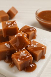 Photo of Tasty caramel candies with sauce and sea salt on white table, closeup