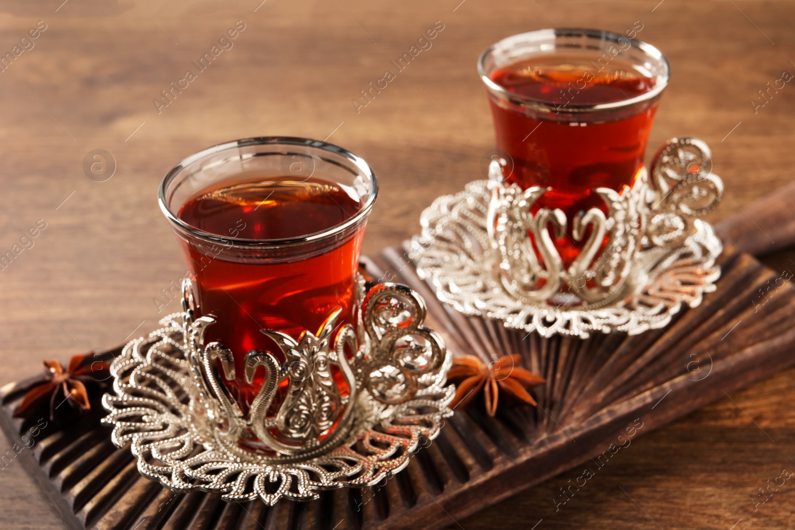 Photo of Glasses of traditional Turkish tea in vintage holders and anise stars on wooden table, closeup