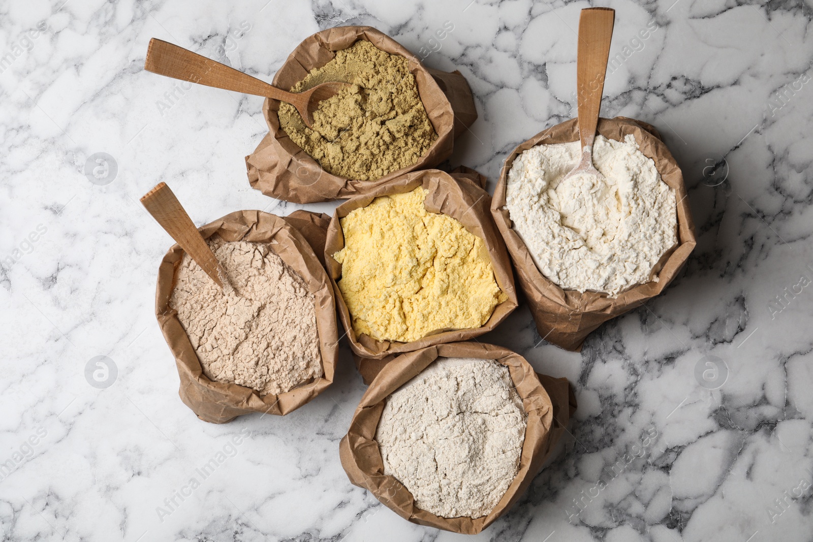 Photo of Paper bags with different types of flour on marble background