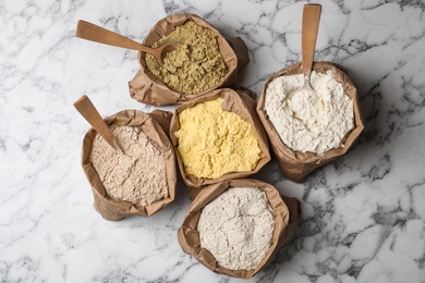 Paper bags with different types of flour on marble background