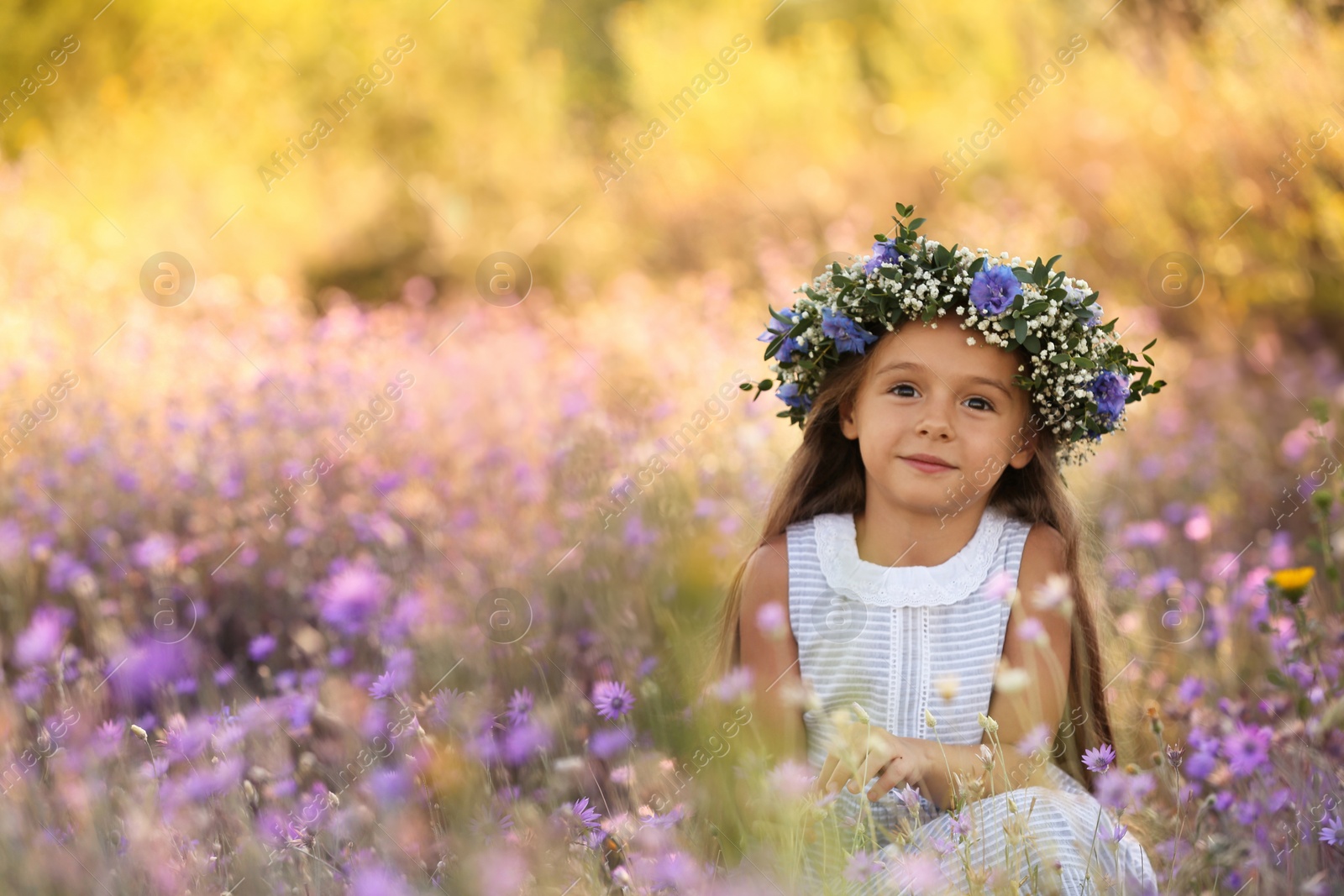 Photo of Cute little girl wearing flower wreath outdoors, space for text. Child spending time in nature