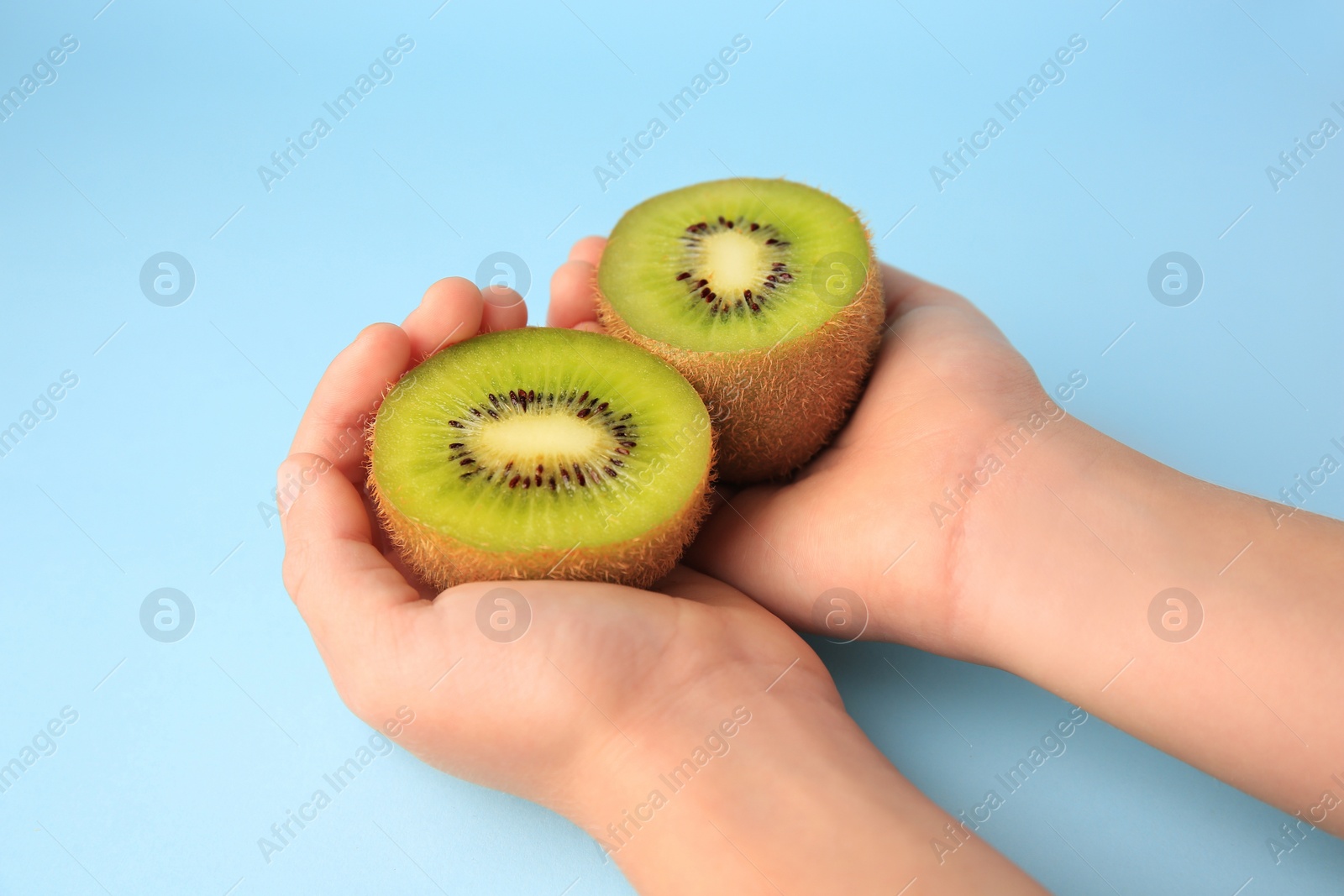 Photo of Woman holding delicious fresh kiwi on light blue background, closeup