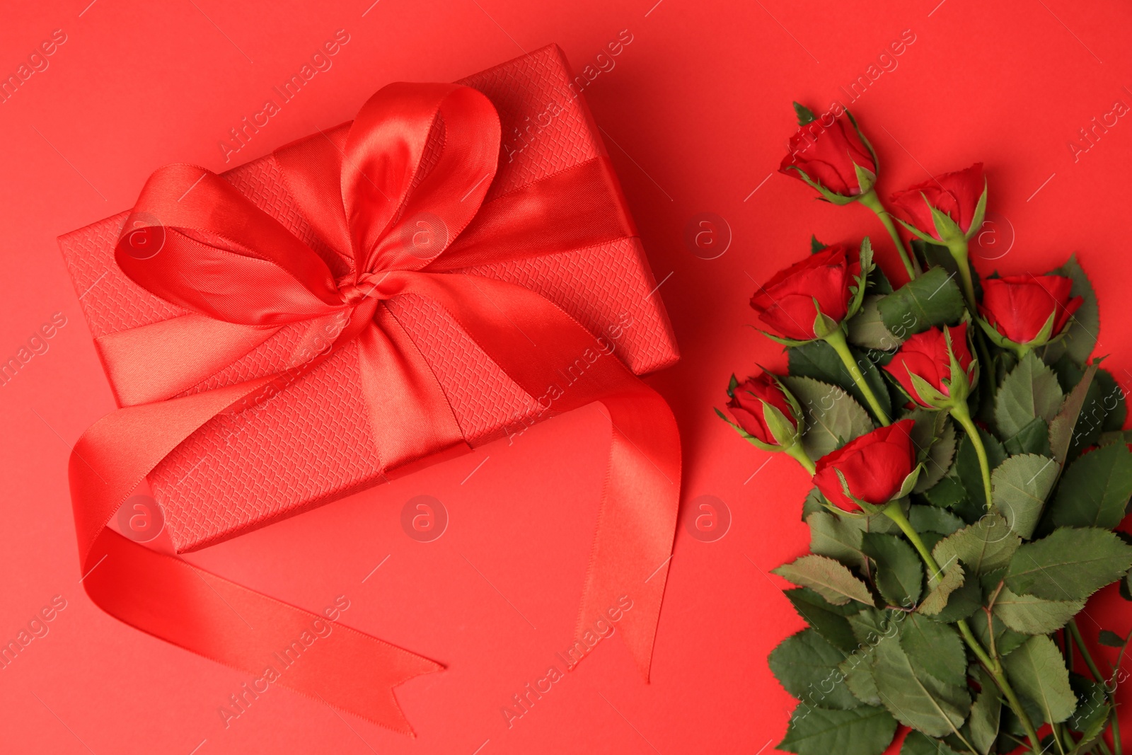 Photo of Beautiful gift box with bow and roses on red background, flat lay