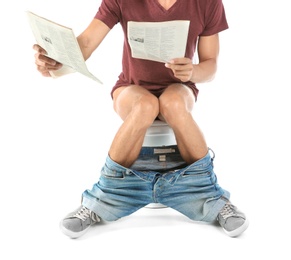 Young man reading newspaper while sitting on toilet bowl. Isolated on white