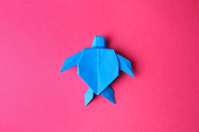 Photo of Origami art. Handmade light blue paper turtle on pink background, top view