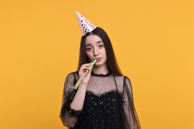 Woman in party hat with blower on orange background