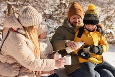 Happy family warming themselves with hot tea outdoors on snowy day