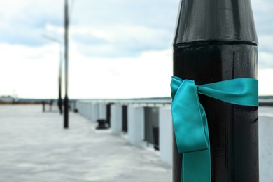 Photo of Teal ribbon tied to street lamp outdoors, space for text