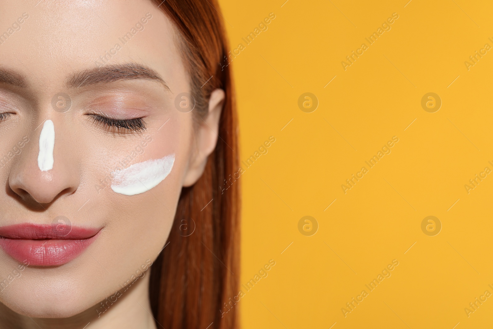 Photo of Beautiful young woman with sun protection cream on her face against orange background, closeup. Space for text