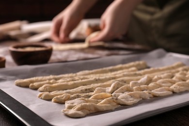 Woman cooking traditional grissini at table, focus on homemade breadsticks with spices