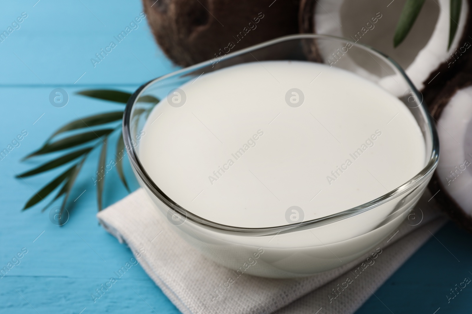 Photo of Bowl of delicious vegan milk, palm leaf and coconuts on light blue wooden table, closeup