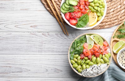 Delicious poke bowls with fish and edamame beans on white wooden table, flat lay. Space for text