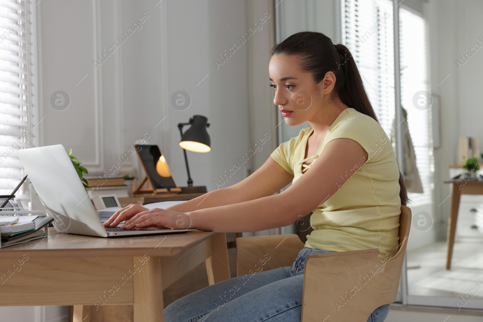 Photo of Young woman with poor posture using laptop at table indoors