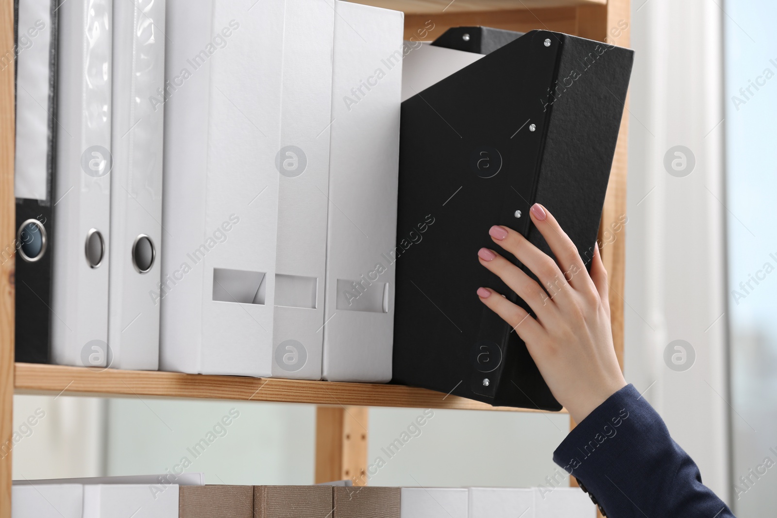 Photo of Woman taking folder with documents from shelf in office, closeup