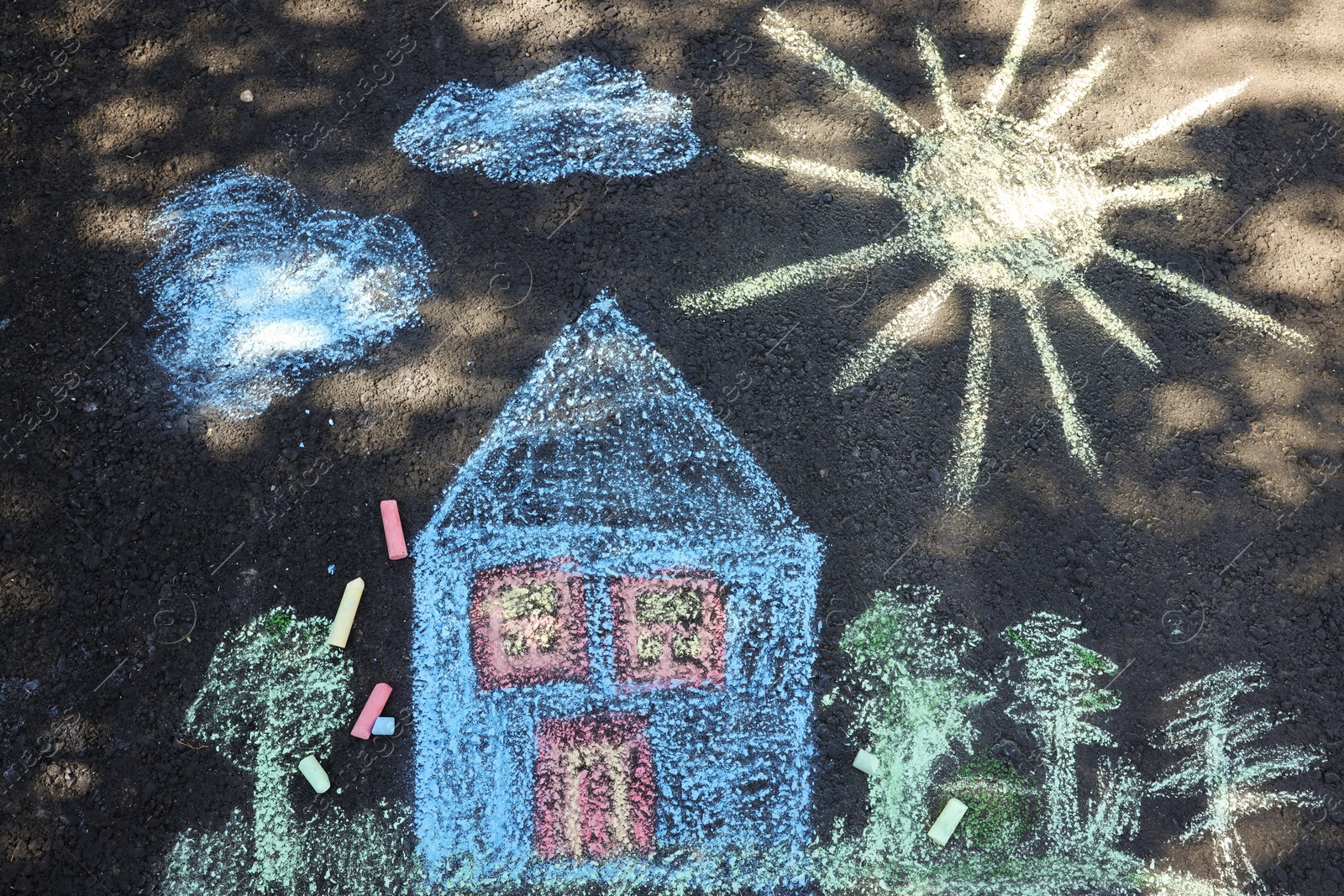 Photo of Child's house drawing and pieces of color chalk on asphalt, flat lay