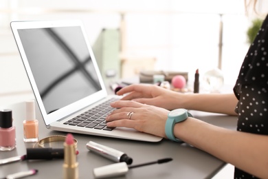 Photo of Young woman with makeup products using laptop at table. Beauty blogger