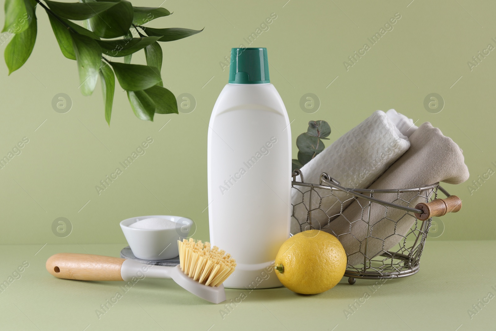 Photo of Bottle of cleaning product, baking soda, lemon and brush on light green background