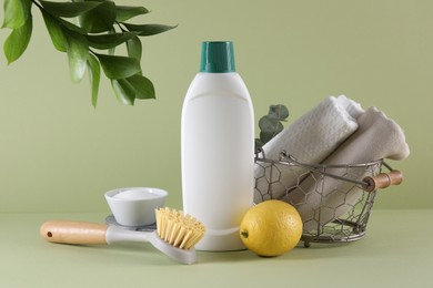 Bottle of cleaning product, baking soda, lemon and brush on light green background