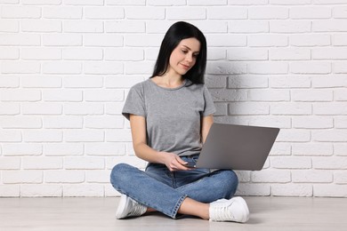 Student with laptop sitting on floor near white brick wall