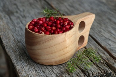 Photo of Cup with tasty ripe lingonberries and spruce twigs on wooden surface, closeup