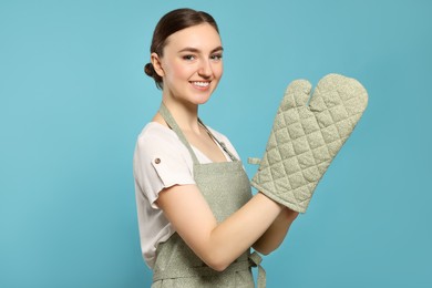 Photo of Beautiful young woman in clean apron with pattern and oven glove on light blue background