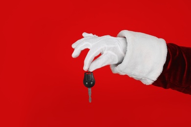 Photo of Santa Claus holding car key on red background, closeup of hand