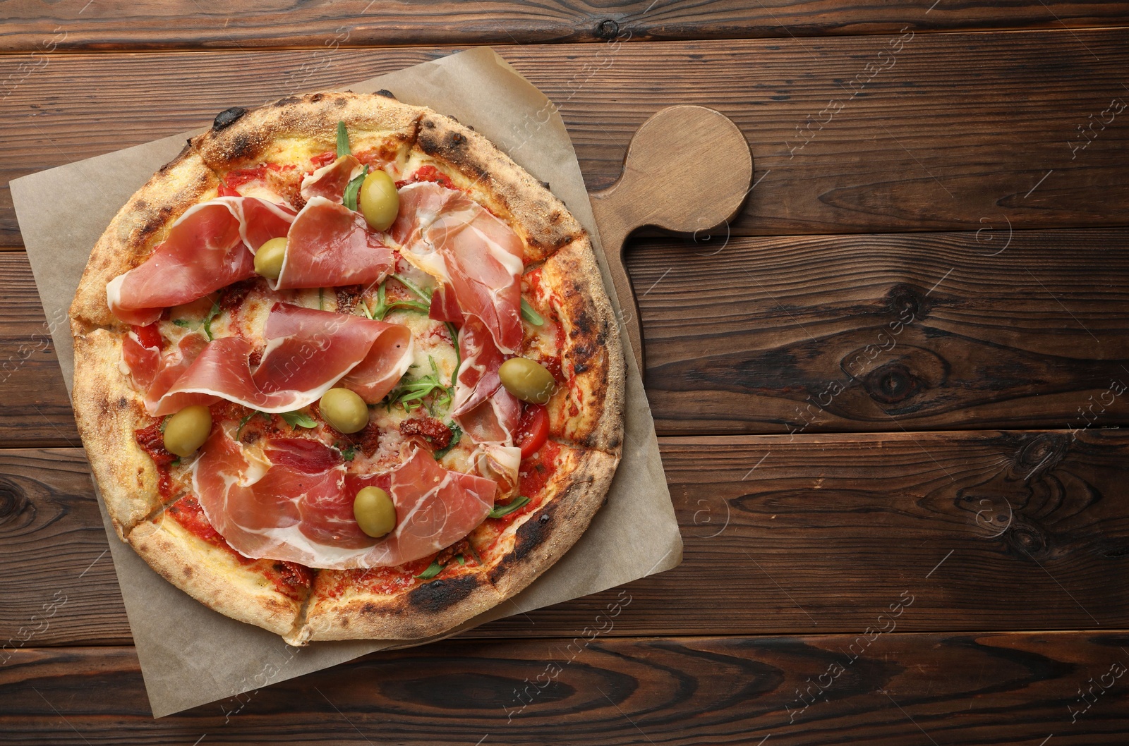 Photo of Tasty pizza with cured ham, olives and sun-dried tomato on wooden table, top view. Space for text