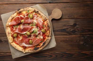 Photo of Tasty pizza with cured ham, olives and sun-dried tomato on wooden table, top view. Space for text