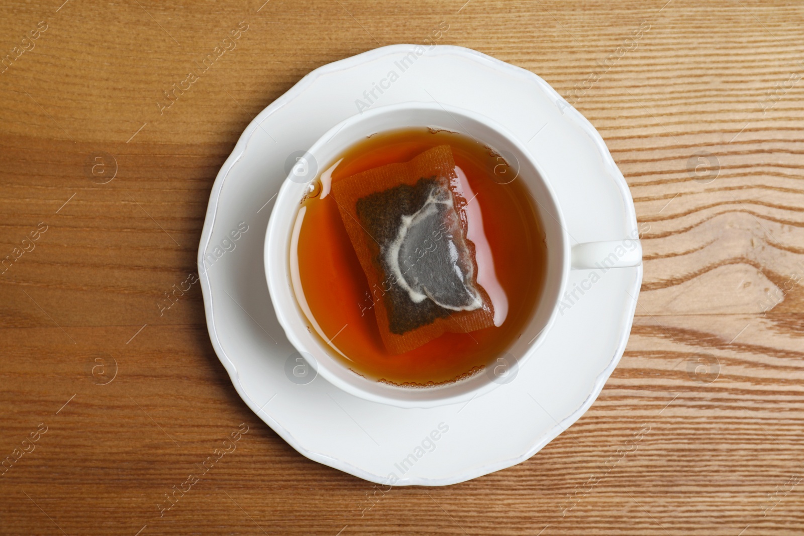 Photo of Cup of hot fresh tea with bag on wooden background, top view