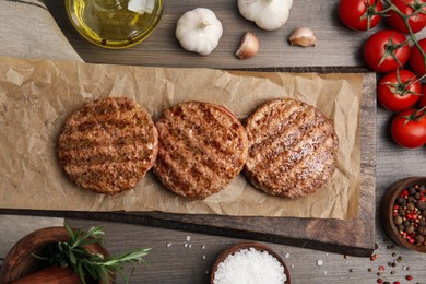 Photo of Board with tasty grilled hamburger patties and seasonings on wooden table, flat lay