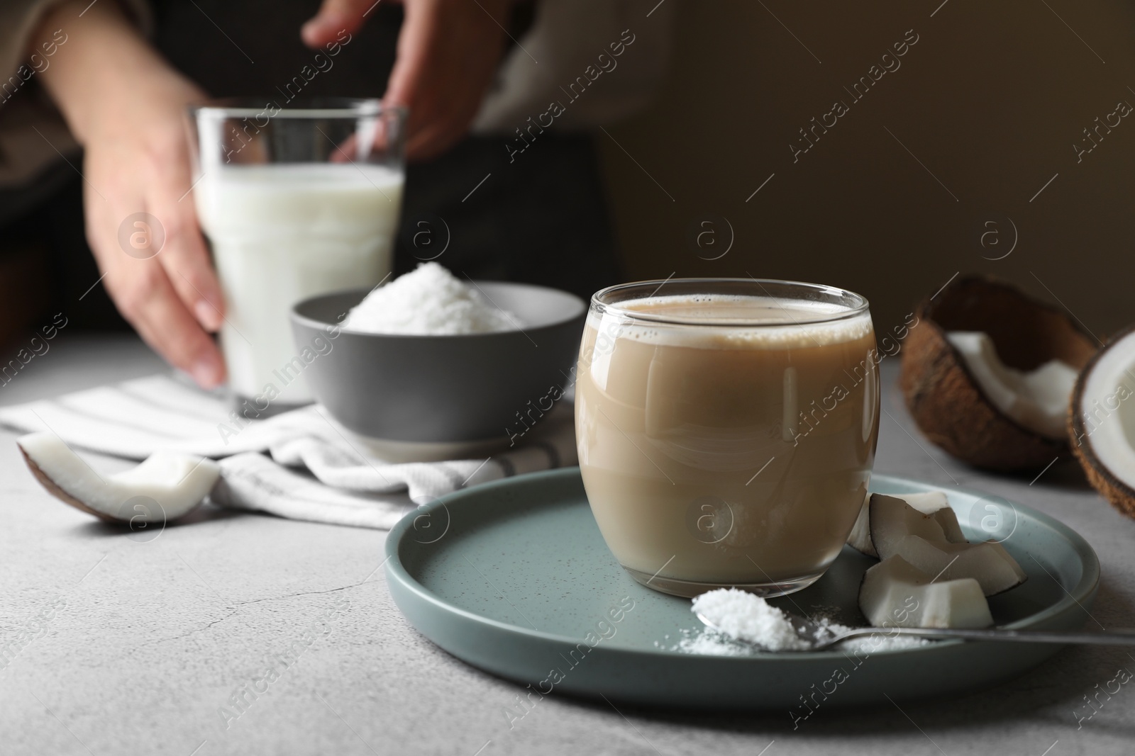 Photo of Glass of coffee with coconut milk, pieces and flakes on light grey table, space for text