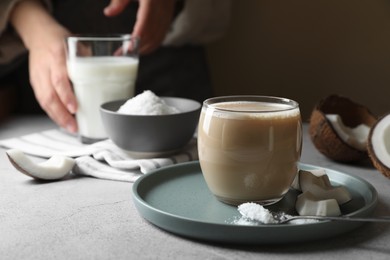 Glass of coffee with coconut milk, pieces and flakes on light grey table, space for text