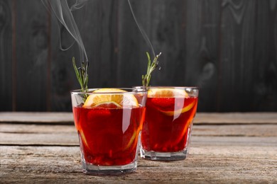 Photo of Glasses of delicious refreshing sangria with smoke on old wooden table