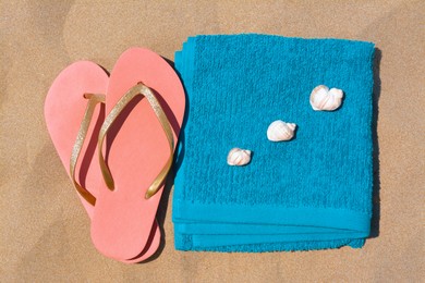 Photo of Folded soft blue beach towel with flip flops, seashells on sand, flat lay
