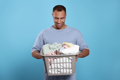 Photo of Happy man with basket full of laundry on light blue background