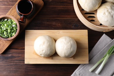 Delicious Chinese steamed buns, green onion and soy sauce on wooden table, flat lay