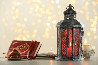 Photo of Arabic lantern, Quran, misbaha, candles and dates on table against blurred lights
