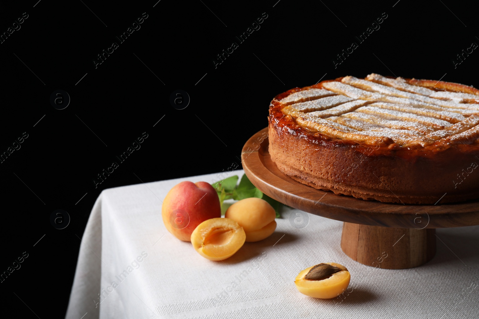 Photo of Tasty apricot pie with powdered sugar on table against black background, space for text