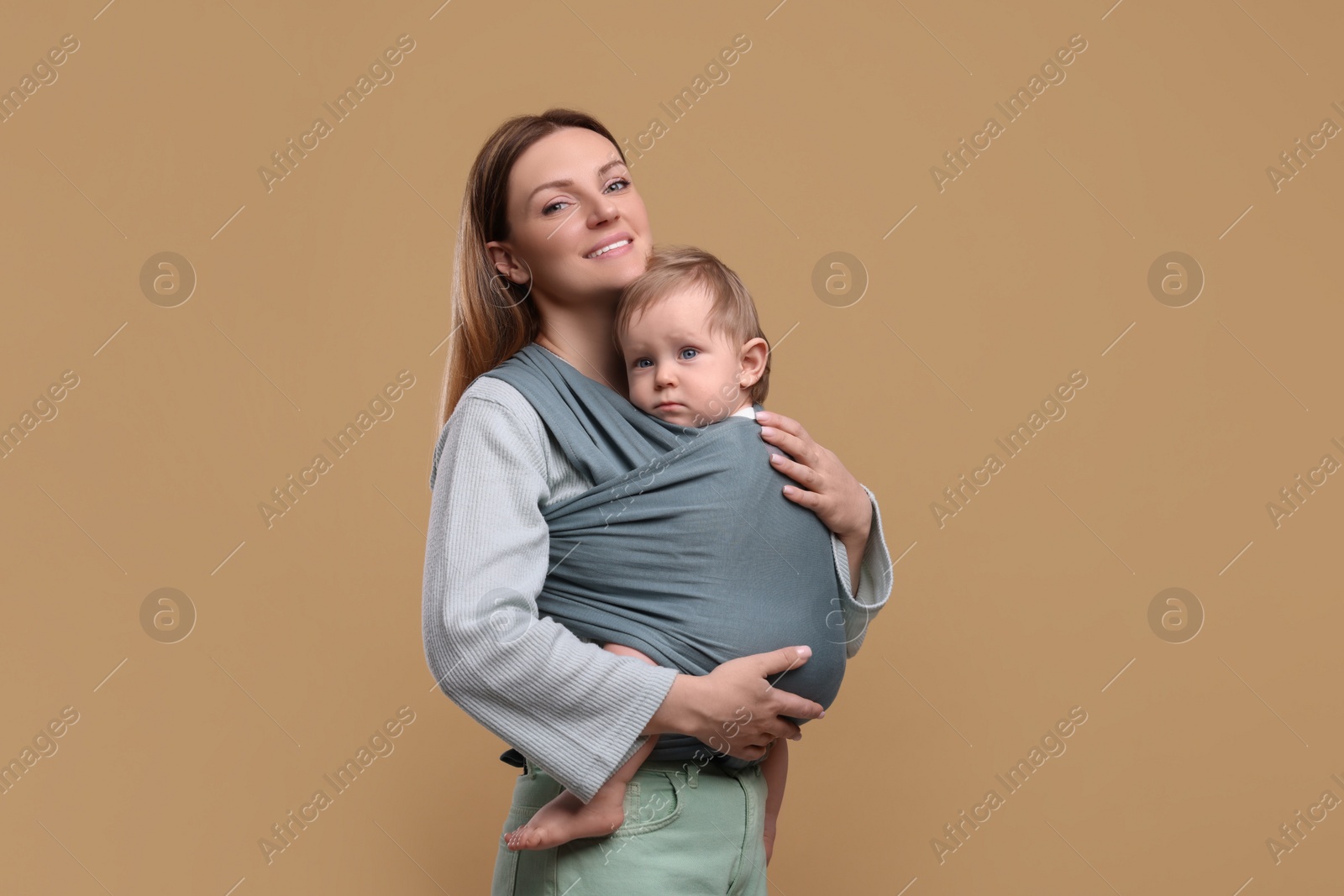 Photo of Mother holding her child in baby wrap on light brown background