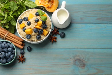 Flat lay composition with bowl of tasty quinoa porridge, blueberries and pumpkin on light blue wooden table. Space for text