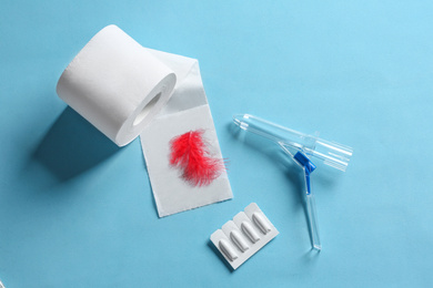 Photo of Anoscope, suppositories and toilet paper with red feather on light blue background, flat lay. Hemorrhoid treatment
