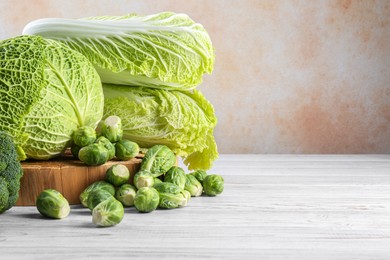 Different fresh cabbages on white wooden table, space for text